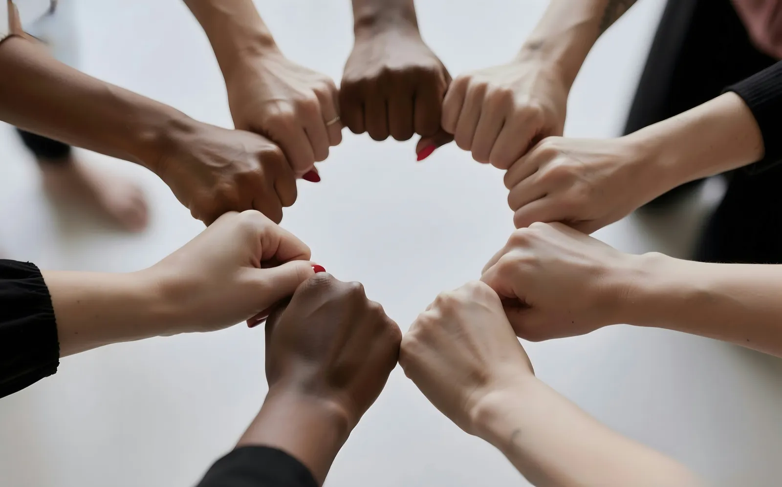 Hands of different skin tones meeting in a circle of fist bumps.